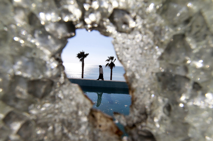 A Tunisian woman, seen through a broken glass window, walks next to the swimming pool at the empty and ransacked home of Kaif Ben Ali, nephew of former President Zine al-Abidine Ben Ali, in Hammamet