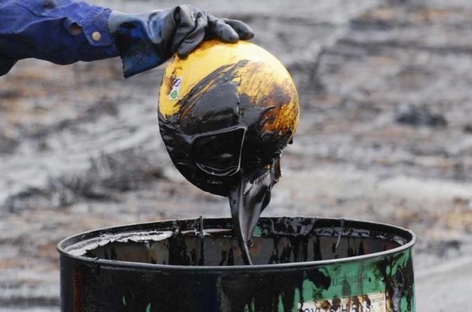 A labourer pours oil that he scooped up from the oil spill with a helmet into an oil drum, near Dalian port, Liaoning province