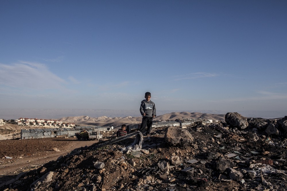 A young boy from Abu Nowar Bedouin community with Ma(***)aleh Adumim settlement in the background. Like Khan al-Ahmar, the community is part of a cluster of Bedouin communities living in or near the E1 corridor, which is slated for expansion. Already served with demolition orders, the 118-person community bides its time.