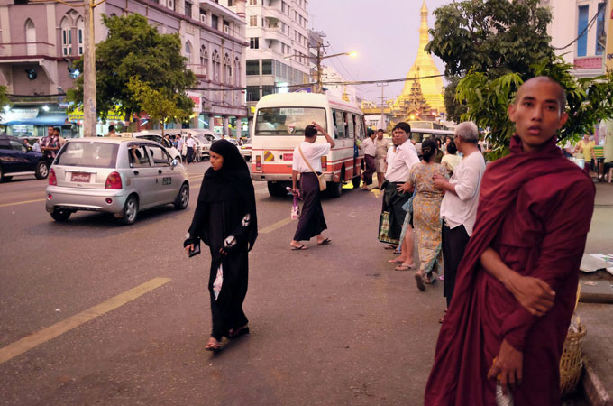 A Muslim woman walks past a young Buddhist monk. The violence has coincided with the growth of the "Buddhist 969" movement, which is frequently tied to attacks against Muslim communities. [Brennan O''Connor/Al Jazeera]