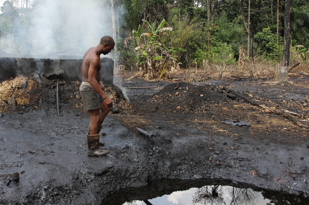 A worker at an illegal refinery camp inspects refinery equipment as smoke emerges from behind drums, near the Nun River in Nigeria(***)s oil state of Bayelsa.