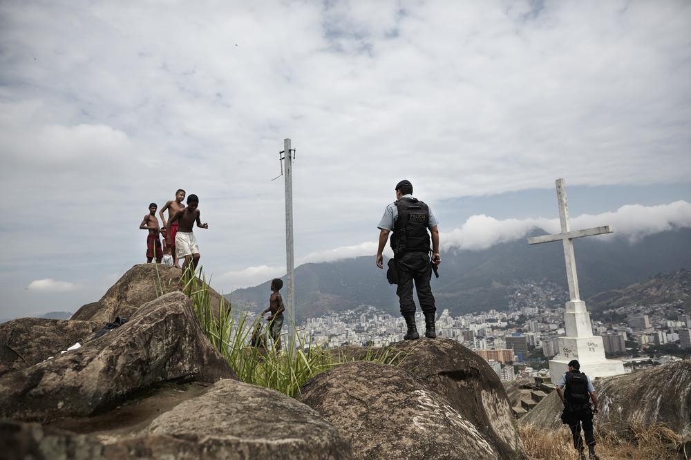 <p>Members of the Pacifying Police Unit (UPP) stand guard while children play on top of the Macaco favela in northern Rio de Janeiro.</p>