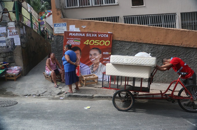 Residents of the Pavao-Pavaozinho favela pass candidate Marina Silva's campaign poster [Flora Charner/Al Jazeera]