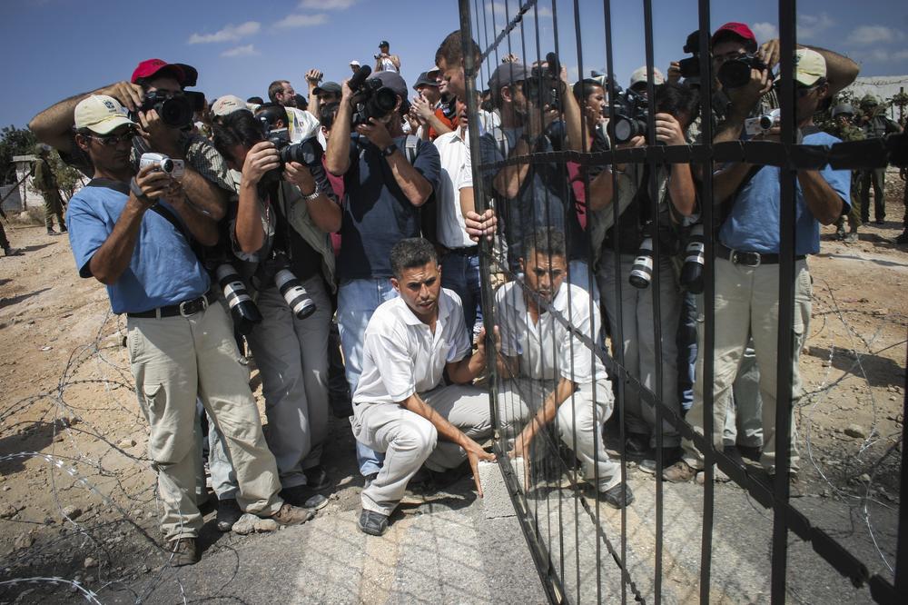 Mohamed Abu-Khatib, a Popular Struggle leader from the village of Bilin holds mirrors in front of Israeli army forces as a performance held during the weekly protest against the wall, in July 2005.