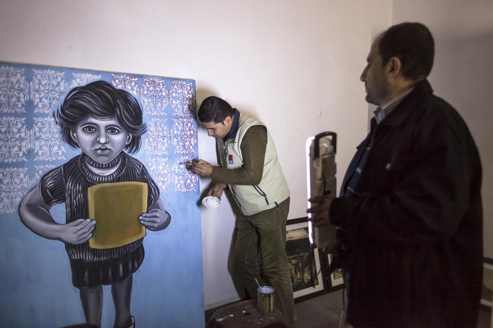 Mohammed Abusal paints at Eltiqah gallery, while fellow artist, Suhail Salem, holds a portable light. Eltiqah gallery was founded in 2001.