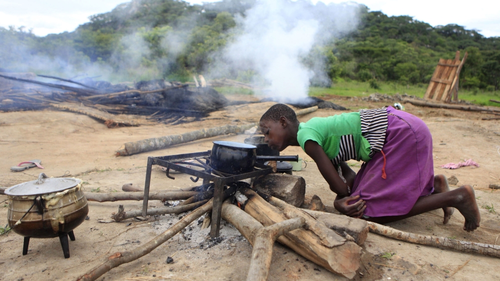 A Zimbabwean girl prepares food besides burnt and demolished makeshift shelters at Manzou Farm in Mazowe [REUTERS]