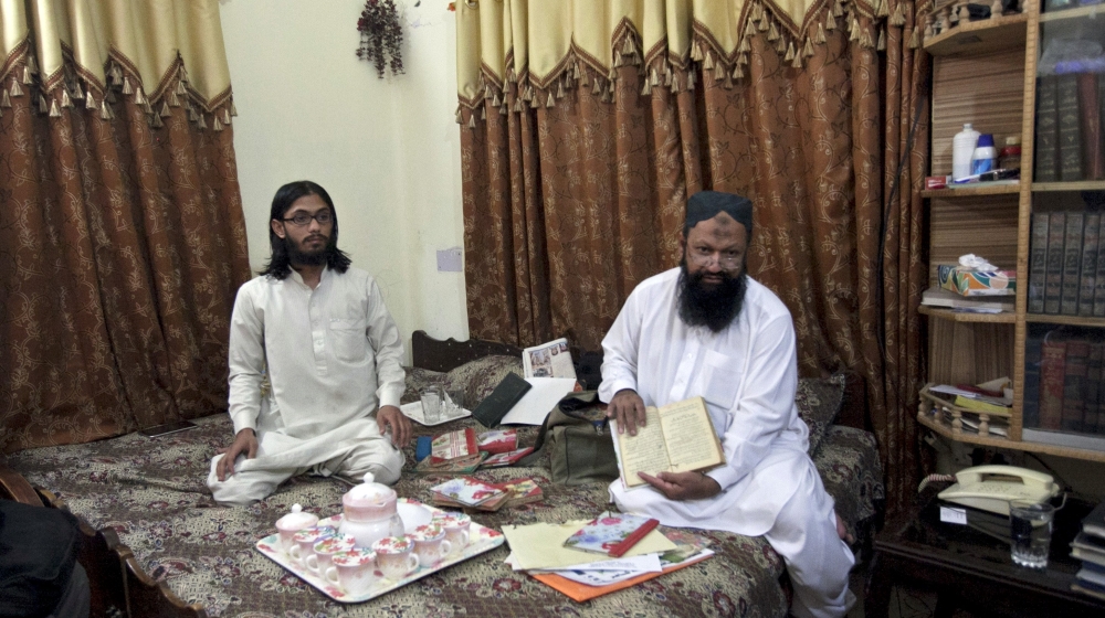 File photo of Leader of the Lashkar-e-Jhangvi Ishaq sitting on a bed with his son Malik Usman as he shows a book during an interview with Reuters at his home in Rahim Yar Khan