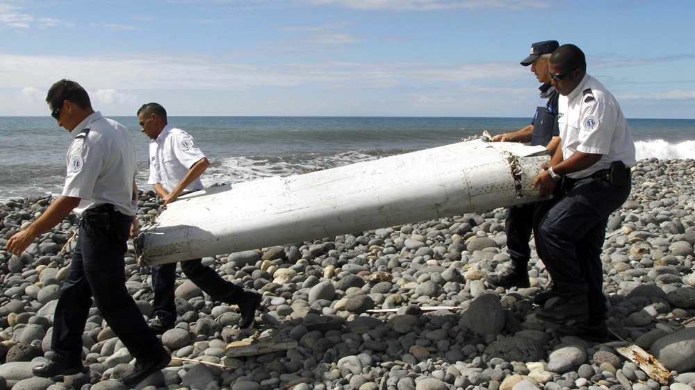 Four men carry a flaperon on a pebbly beach on Reunion Island. It was later identified as from MH370