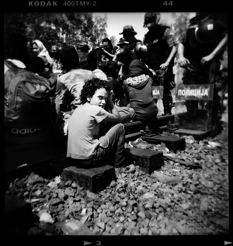 A refugee boy sits on the Greek side of the border beside Macedonian special forces who are guarding the border with Greece near the village of Idomeni - Idomeni, Greece, August 2015 [Giorgos Moutafis] 
