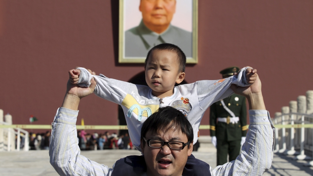 A boy sits on his father''s shoulders as they pose for a photograph in front of the giant portrait of late Chinese chairman Mao Zedong on the Tiananmen Gate, in Beijing