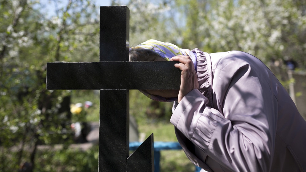 The mother of Andrey Papov, who died in a mining accident at the age of 34, kisses his grave on the first Sunday after Easter, when Russian Orthodox families visit their dead relatives. [Janos Chiala and Tali Mayer/Al Jazeera]  