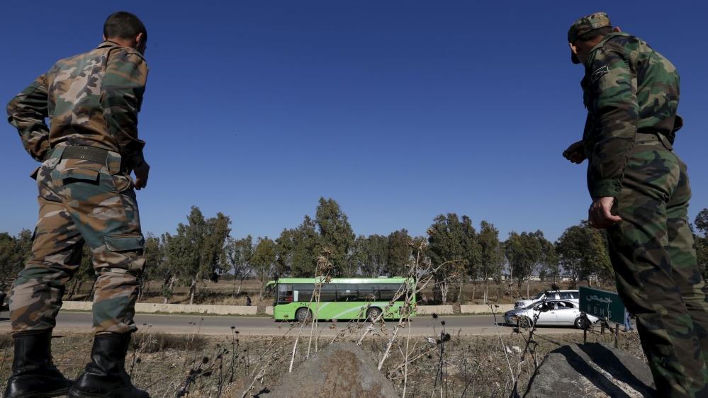 Syrian Army forces look on as buses leave Al Waer neighbourhood during a truce between the government and rebels in Homs [Reuters]