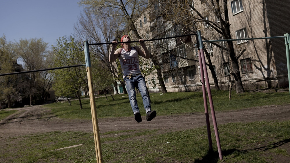 Twenty-seven-year-old Andrej plays a game of lientochka in Krasnodon. This is when two people challenge each other to do a certain number of pull-ups, adding one more at each turn. His opponent gave up when they reached 11 so Andrej continued on his own. [Janos Chiala and Tali Mayer/Al Jazeera]  