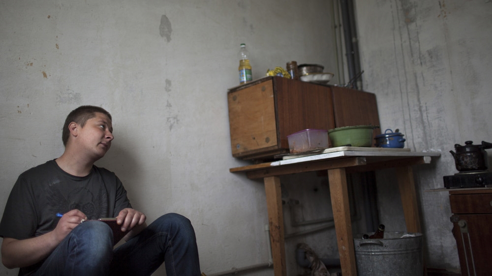 Thirty-year-old Sasha draws in the kitchen of his flat in Shakhtiorsk. He cannot work because of internal injuries he suffered in a mining accident, and therefore has no money. His boss claimed the accident was Sasha's fault and refused to pay him compensation. [Janos Chiala and Tali Mayer/Al Jazeera]  