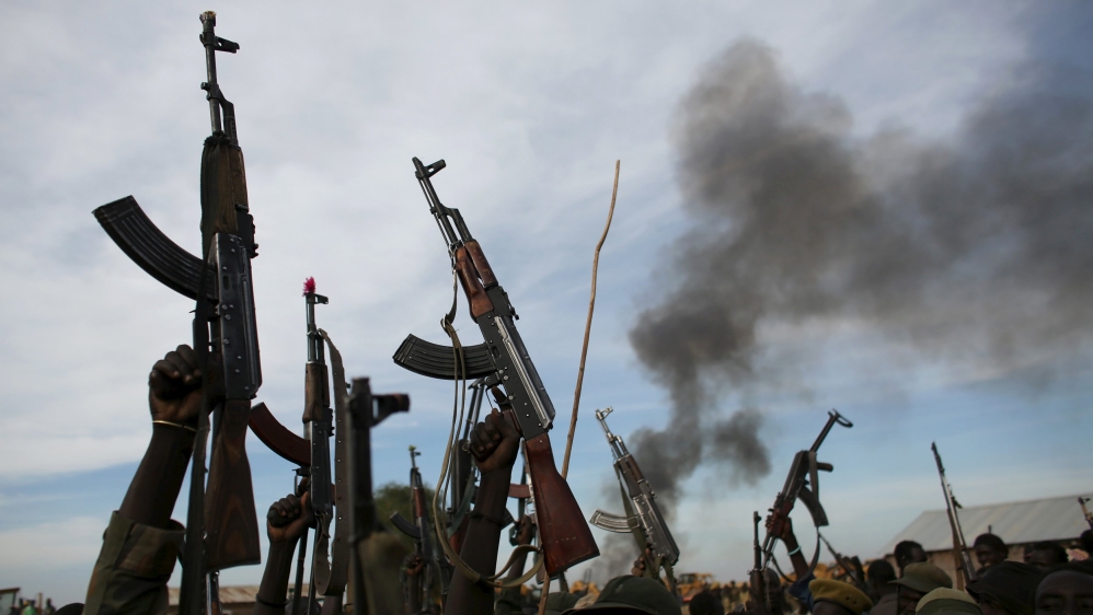 Rebel fighters hold up their rifles as they walk in front of a bushfire in a rebel-controlled territory in Upper Nile State