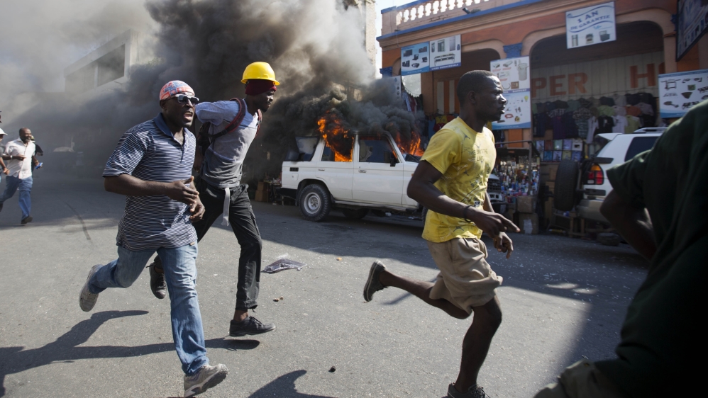Protesters run past a burning car during a protest against President Michel Martelly''s government