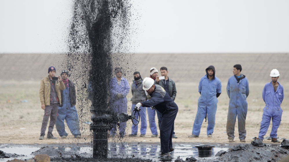 Iraqi workers stand near a pipeline as it ejects oil at Al Tuba oil field in Basra