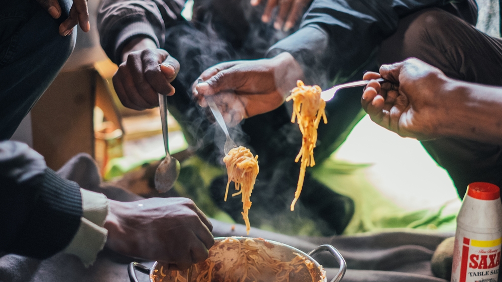 Adam, Aman, John and two other Eritrean refugees eat lunch made from volunteer-donated food as they face an uncertain future in Calais [James Rippingale/Al Jazeera] 