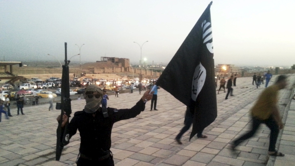 An ISIL fighter holds an ISIL flag and a weapon on a street in the city of Mosul, Iraq [REUTERS]