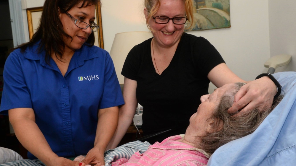 As a teenager during the Second World War, Francoise Levinthal was a member of the French Resistance. She was imprisoned in a concentration camp, but later earned her PhD and became a tenured professor at Columbia University. In this photo, Levinthal, 90, is resting at home as her daughter brushes her hair and Dolores Navarro, an MJHS Hospice nurse, visits [Courtesy of MJHS]