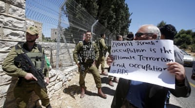 A Palestinian holds a placard during a demonstration against the taking over of land by Israeli authorities to build roads for settlers [EPA]