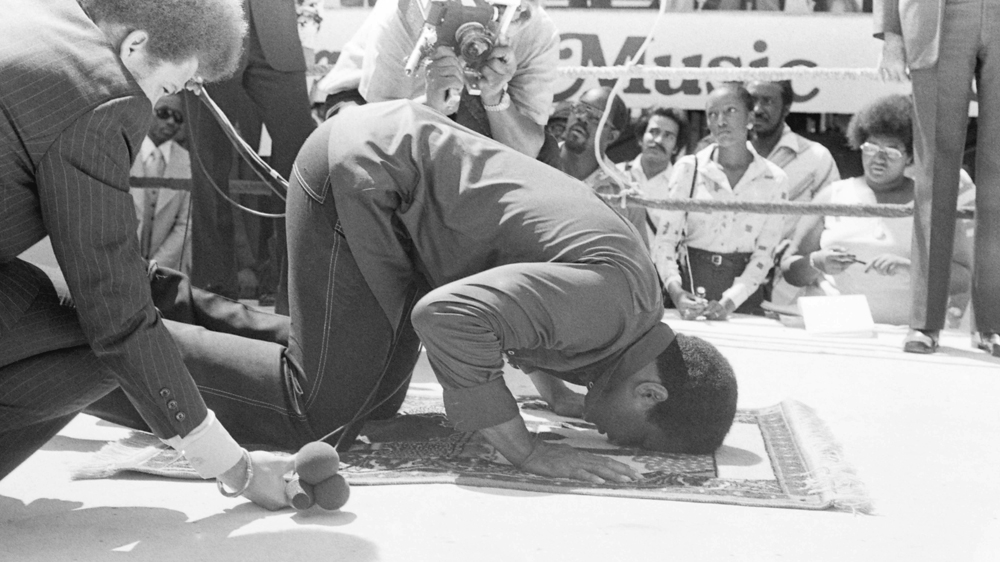Muhammad Ali prays at a press conference before his fight against Ken Norton [File:  August 4, 1976 -   The Ring Magazine/Getty Images]