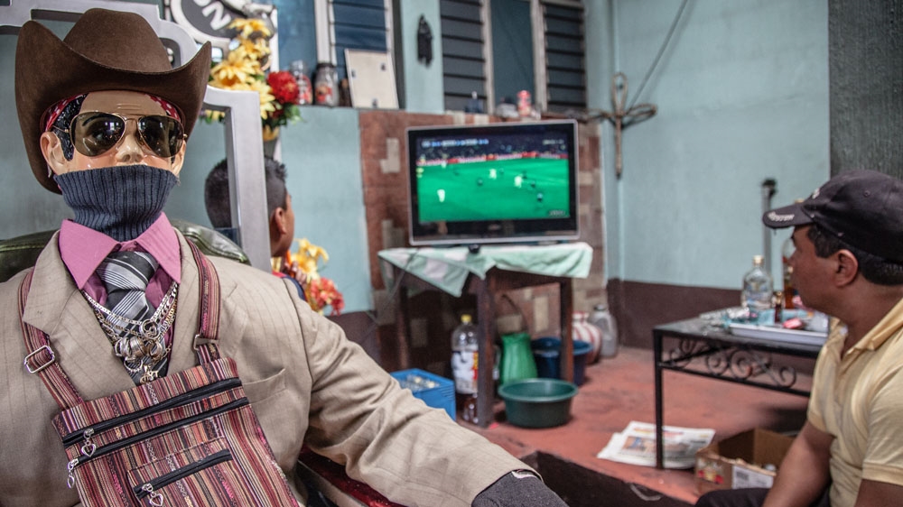 San Simon/Maximon sits behind the shrine along with his attendants. Although there are many variations, he is typically portrayed in a cowboy hat and sunglasses [ Gabriela Campos/Al Jazeera]  
