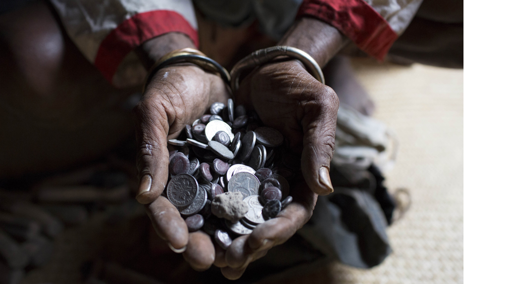 Traditional healer Mbola Tohamana shows his collection of coins, both Malagasy Ariary and old francs, which he uses in diagnosing ailments [Tom Maguire/Al Jazeera]
