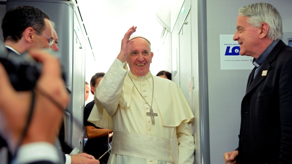 Pope Francis waves next to newly-retired Father Federico Lombardi during a press conference on a plane after the Pope''s visit to Krakow for the World Youth Days