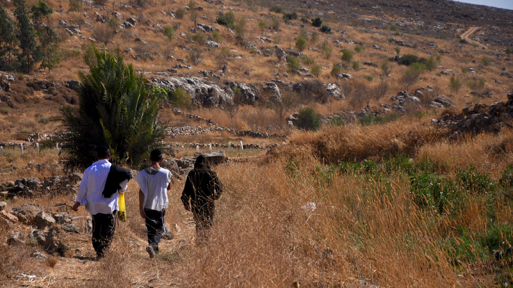 Israeli settlers from the illegal Beit Ein settlement walk through farmland belonging to Wadi Fukin residents after visiting a natural spring on private Palestinian land [Emily Mulder/Al Jazeera]