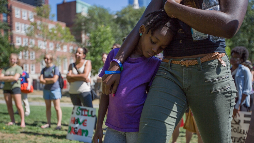 Bria Small, centre, leans against her sister, Naria Sealy, as they listen to Rahsaan Hall speak  [Carolyn Bick/Al Jazeera]  