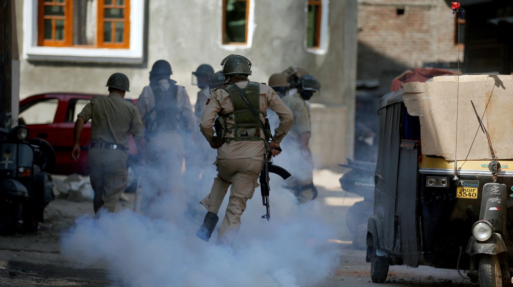 An Indian policeman runs amid tear gas smoke during a protest against the recent killings in Kashmir region, in Srinagar