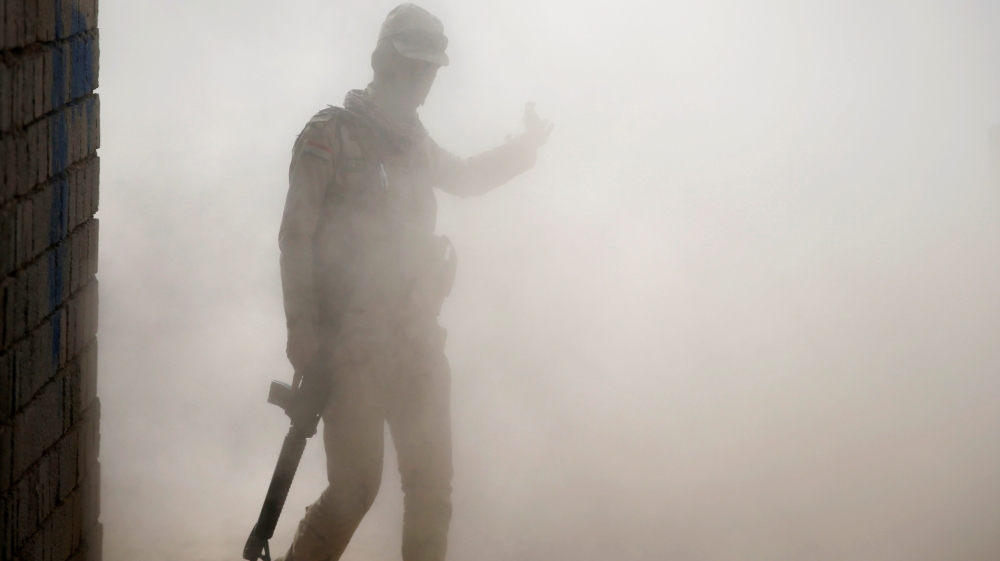 An Iraqi soldier walks through dust in a village outside Mosul