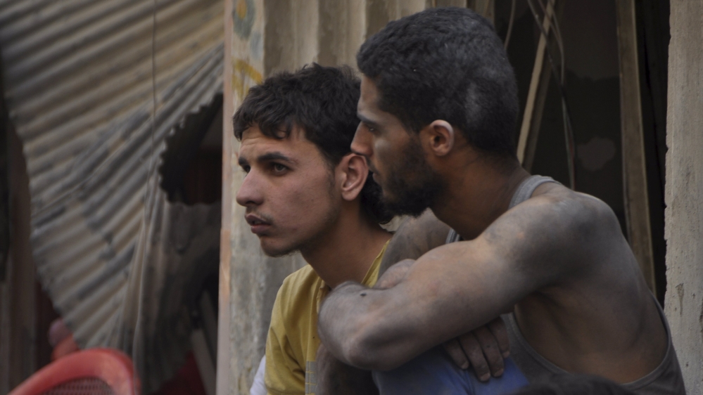 Dust-covered men sit at a site hit by what activists said were barrel bombs thrown by forces loyal to Syria''s President Bashar Al-Assad, in the Palestinian Yarmouk refugee cam