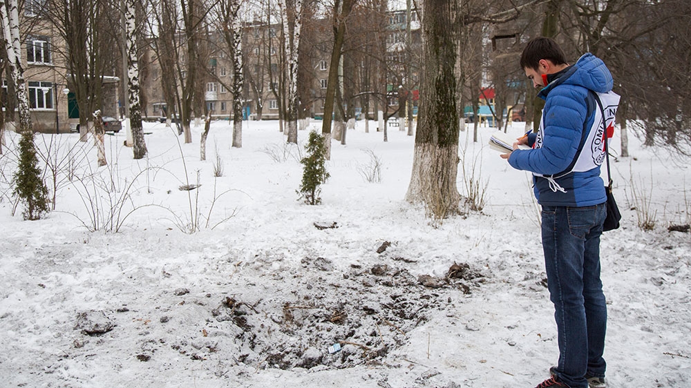 A member of the International Committee of the Red Cross examines a crater made by a mortar the night before in front of School Number 2 in central Avdiivka [John Wendle/Al Jazeera]