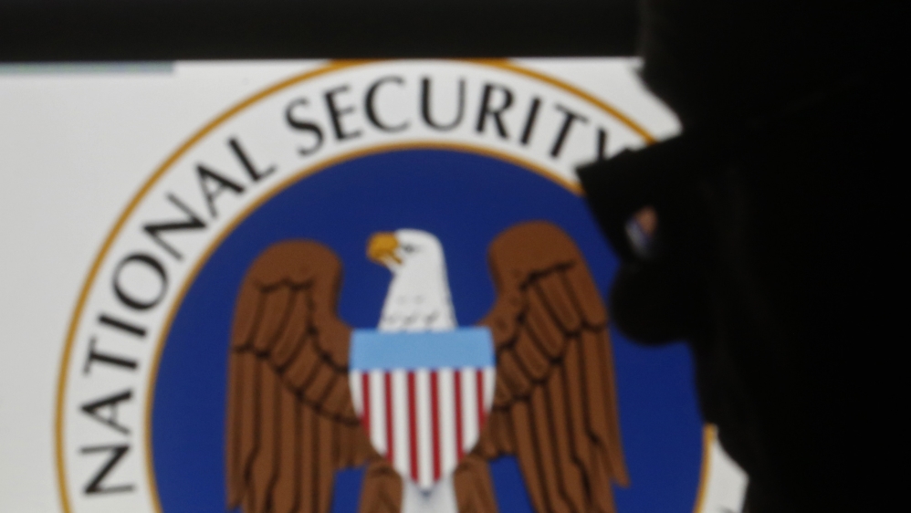 A man is silhouetted near logos of the U.S. National Security Agency (NSA)
