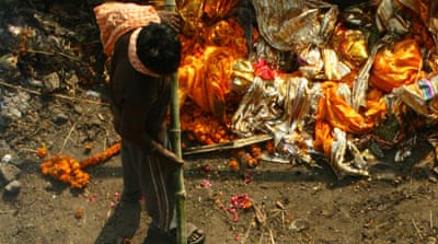 A Dom tends to a cremation, while behind him lie abandoned shrouds, like the ones Yogi and his friends would steal as children and sell to shopkeepers who would wash, iron and resell them in glossy, transparent packets to mourning customers. [Radhika Iyengar/Al Jazeera]