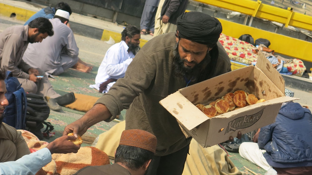 A volunteer hands out cakes to sit-in attendees who spent the night camped out on a major highway [Asad Hashim/Al Jazeera]