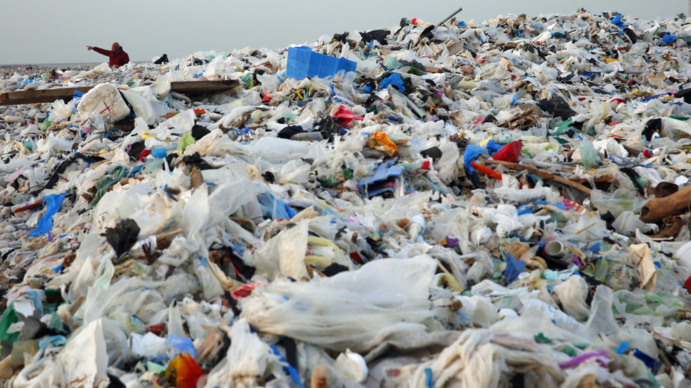 A man gestures as he walks along a shore covered with garbage [Hussein Malla/AP]