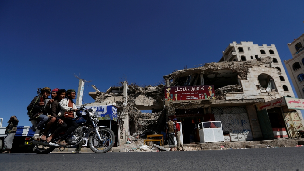 People ride a motorbike past a building hit by air strikes two years ago in Sanaa