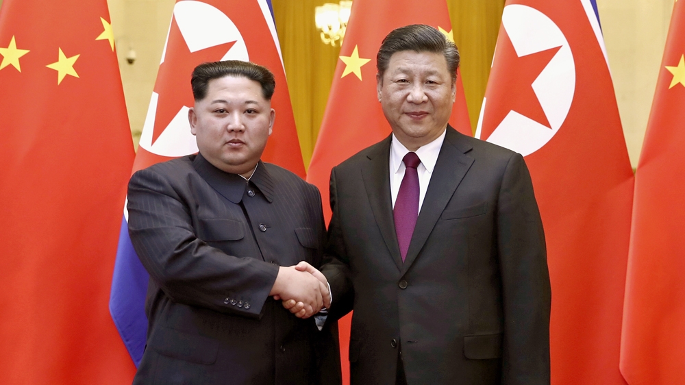 North Korean leader Kim Jong Un and Chinese President Xi Jinping shake hands in front of Chinese and North Korean flags in Beijing, China.