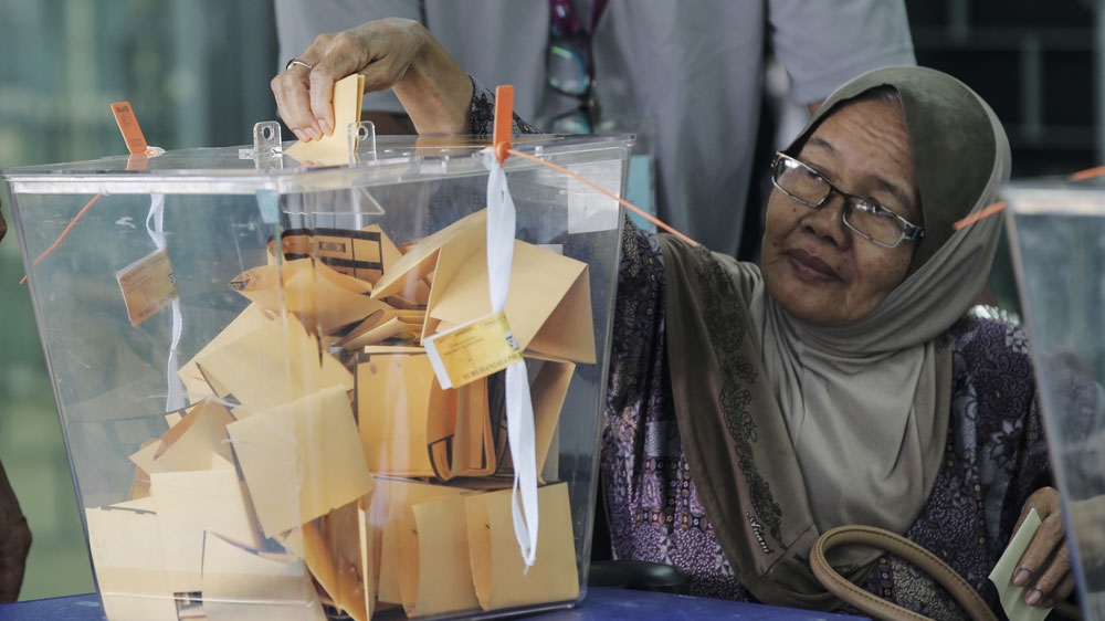 Women puts her yellow ballot paper into a see-through tub which contains other folded papers