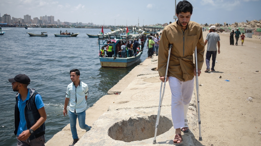 One of the injured in the Great March of Return walks along the Gaza's seaport to watch the boats sail off [Hosam Salem/Al Jazeera]