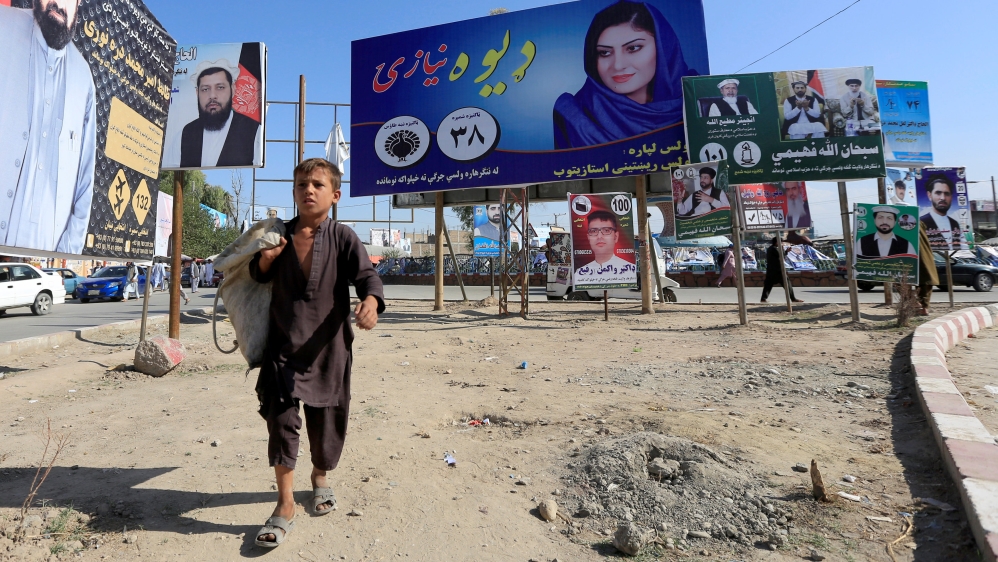 Election posters of parliamentary candidates are installed on a street while a boy walks past in Jalalabad