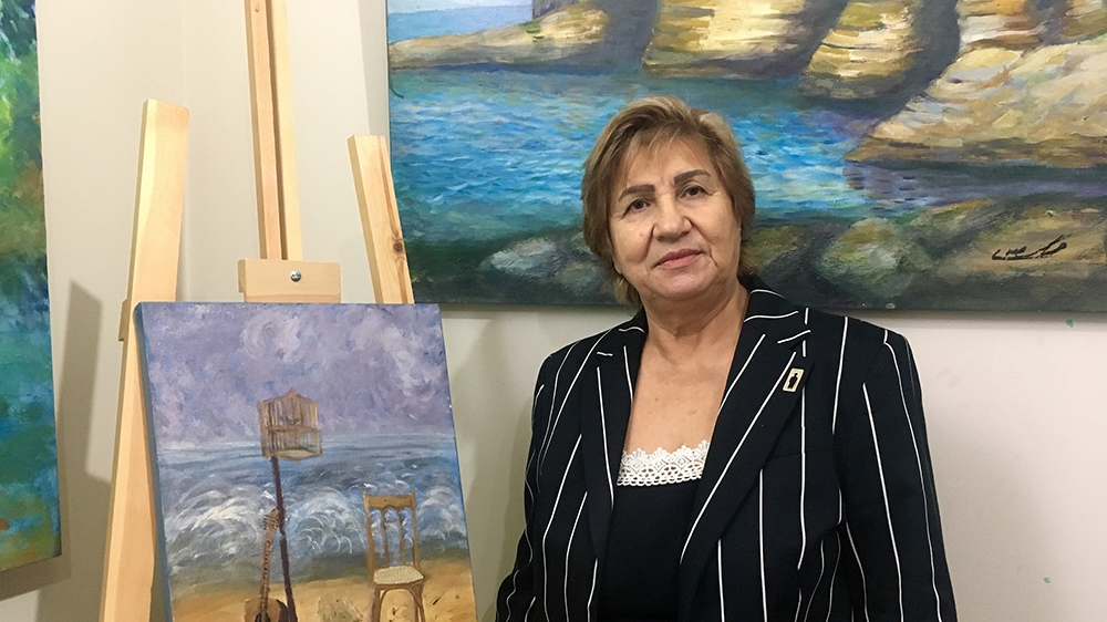 Mariam Saidi, whose son disappeared in 1982, stands in front of a painting she made to exemplify the absence of her child. On her jacket, a small brooch which represents the void let by the disappeare