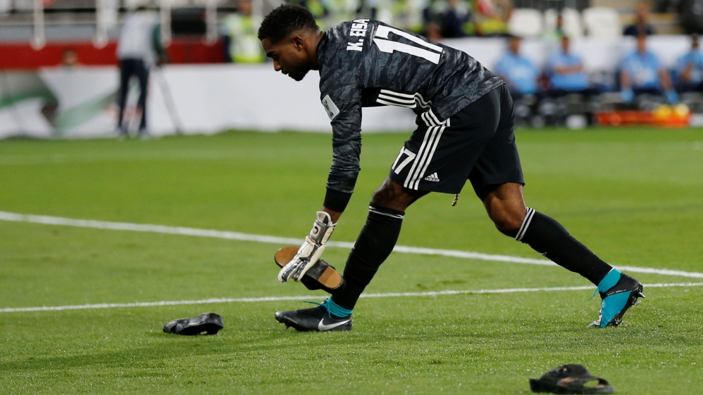 UAE goal-keeper Khalid Eisa clears shoes thrown on the field at Qatari players by the crowd [Thaier Al-Sudani/Reuters]