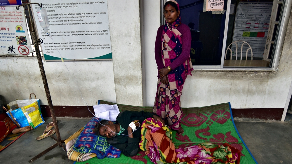 The wife of a tea plantation worker looks on as she stands next to her husband being treated in a corridor of a government hospital in Golaghat [Anuwar Hazarika/Reuters]