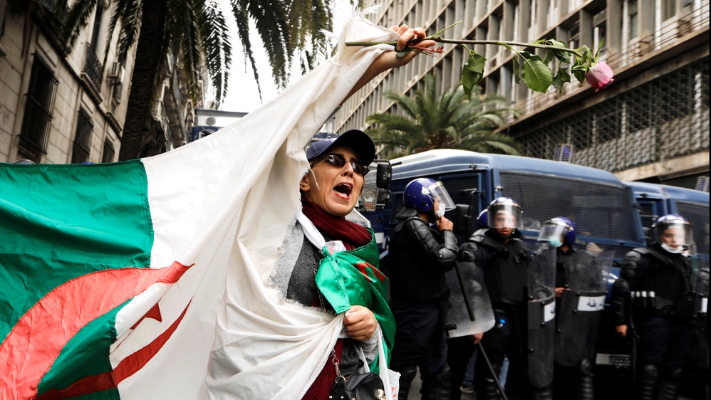 Police members stand guard as a woman carries a flower and a national flag during a protest against President Abdelaziz Bouteflika, in Algiers, Algeria March 8, 2019