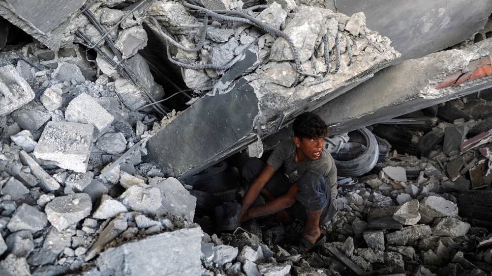 A Palestinian youth searches for his belongings under the rubble of a building that was destroyed by Israeli air strikes, in Gaza [Mohammed Salem/Reuters]
