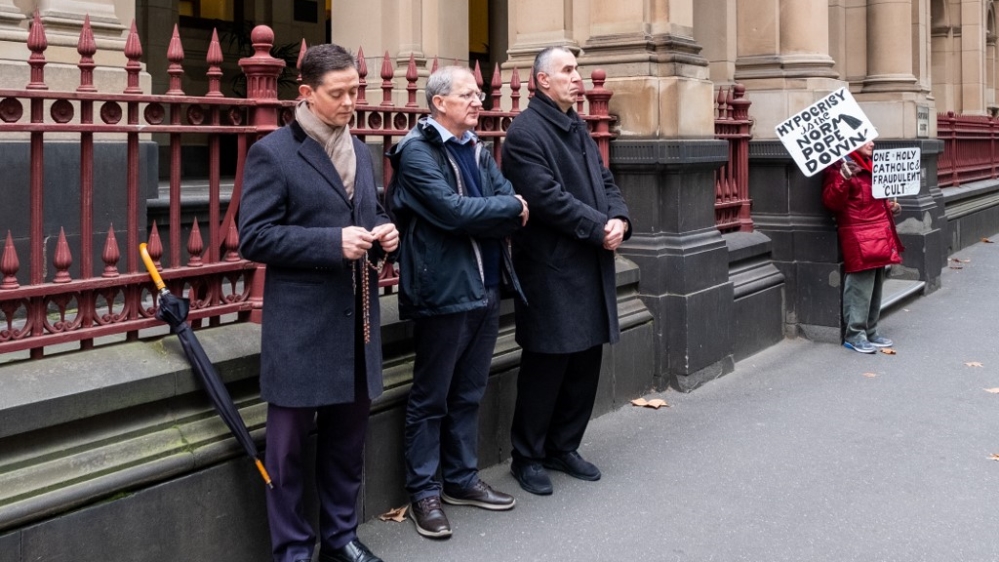 Supporters of Australian Cardinal George Pell (L) pray as a protester against the Catholic church protests outside the Victorian supreme court